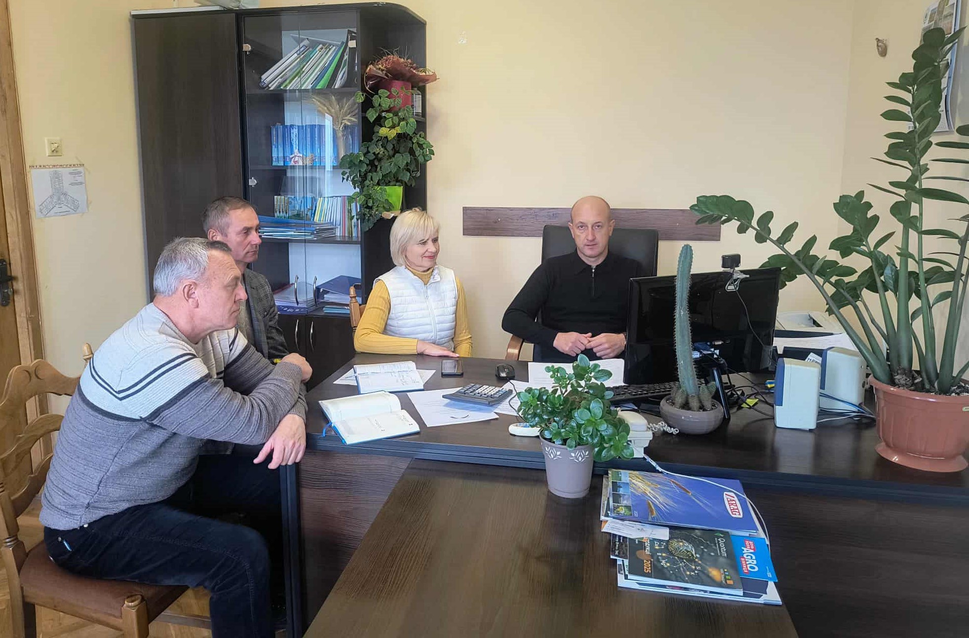  В кабінеті за робочим  столом сидят працівники, перед ними монітор комп'ютера та записники