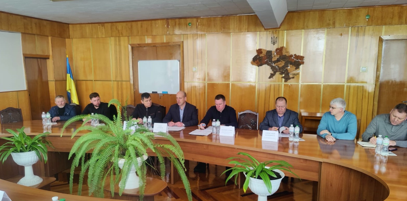 Учасники заходу сидят в залі за робочим столом 