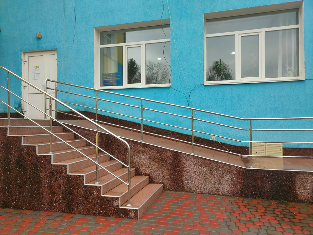 Будівля синього кольору, вхідна група якої обладнана пандусом та сходами коричневого відтінку
