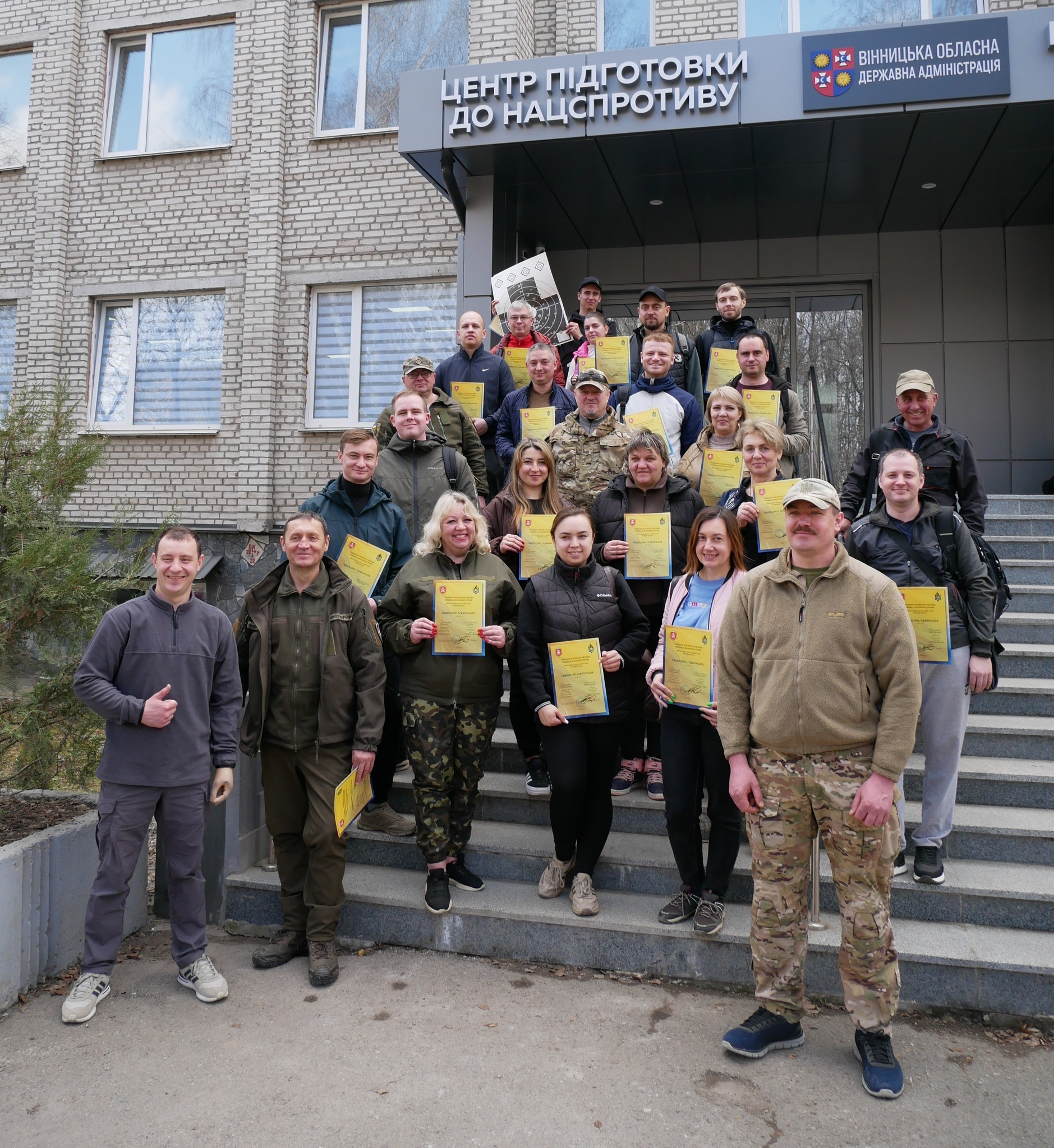 Група людей стоїть біля входу до центу підготовки до нацспротиву з сертифікатами у руках