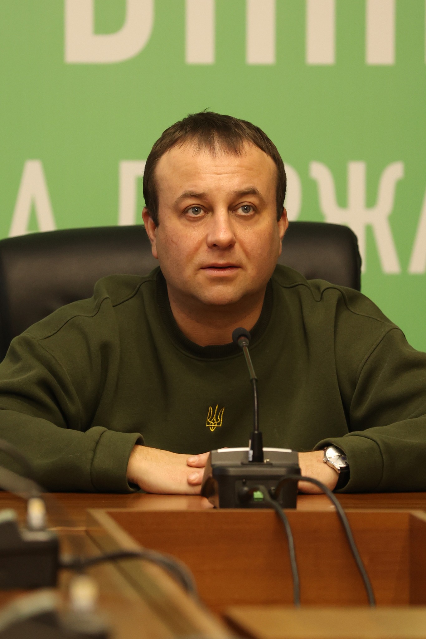 Чоловік сидить за столом з мікрофонами перед собою.