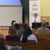 Люди у залі. Керівник Департаменту охорони здоров'я доповідає на сцені