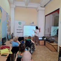 Люди працюють за комп'ютерами, встановленими на столах у навчальному класі і слухать викладача