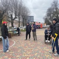 Група з 5–7 осіб, включаючи учасника на візку та людину на милицях, повільно рухається тротуаром, слухаючи гіда.