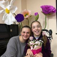 Дівчинка в інвалідному візку тримає квітку разом з жінкою, обидві усміхаються