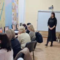 Люди працюють за комп'ютерами, встановленими на столах у навчальному класі і слухать викладача