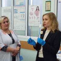 Жінка в синіх рукавичках розповідає щось жінкам у білих халатах