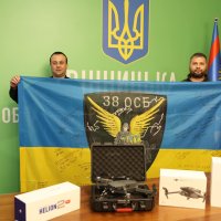 Начальник ОВА Сергій Борзов та учасник передачі Мавіків та тепловізорів військовим тримають у руках прапор України