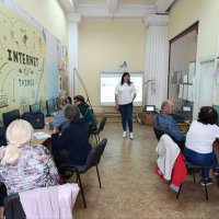 Люди працюють за комп'ютерами, встановленими на столах у навчальному класі і слухать викладача