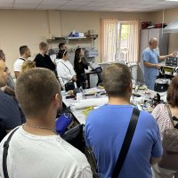 Доповідач веде жваву бесіду (або дискусію) з групою з десяти осіб, які стоять, утворивши півколо